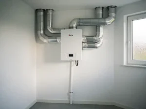 WTW warmteterugwinunit op muur in Nederlandse woning met geïsoleerde zilveren luchtkanalen en condensafvoer.