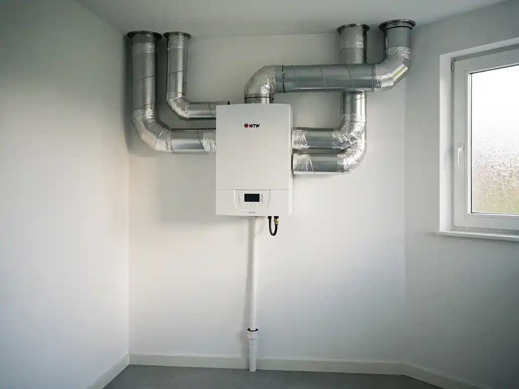 WTW warmteterugwinunit op muur in Nederlandse woning met geïsoleerde zilveren luchtkanalen en condensafvoer.