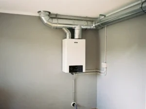 WTW warmteterugwinunit gemonteerd op muur in technische ruimte, met geïsoleerde zilveren kanalen naar het plafond en condensafvoer.